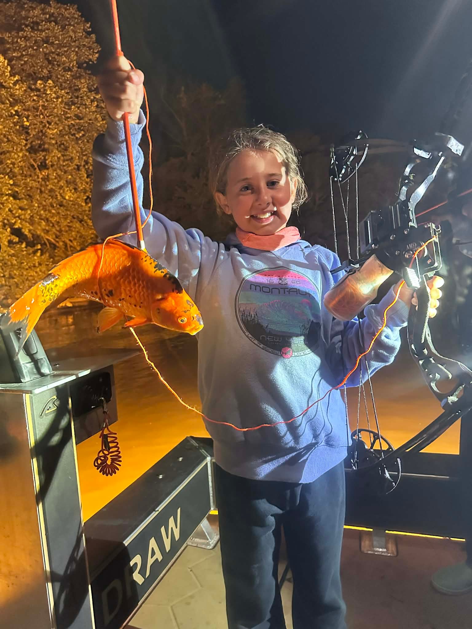 Young angler holding a golden koi on a bowfishing arrow with a bow