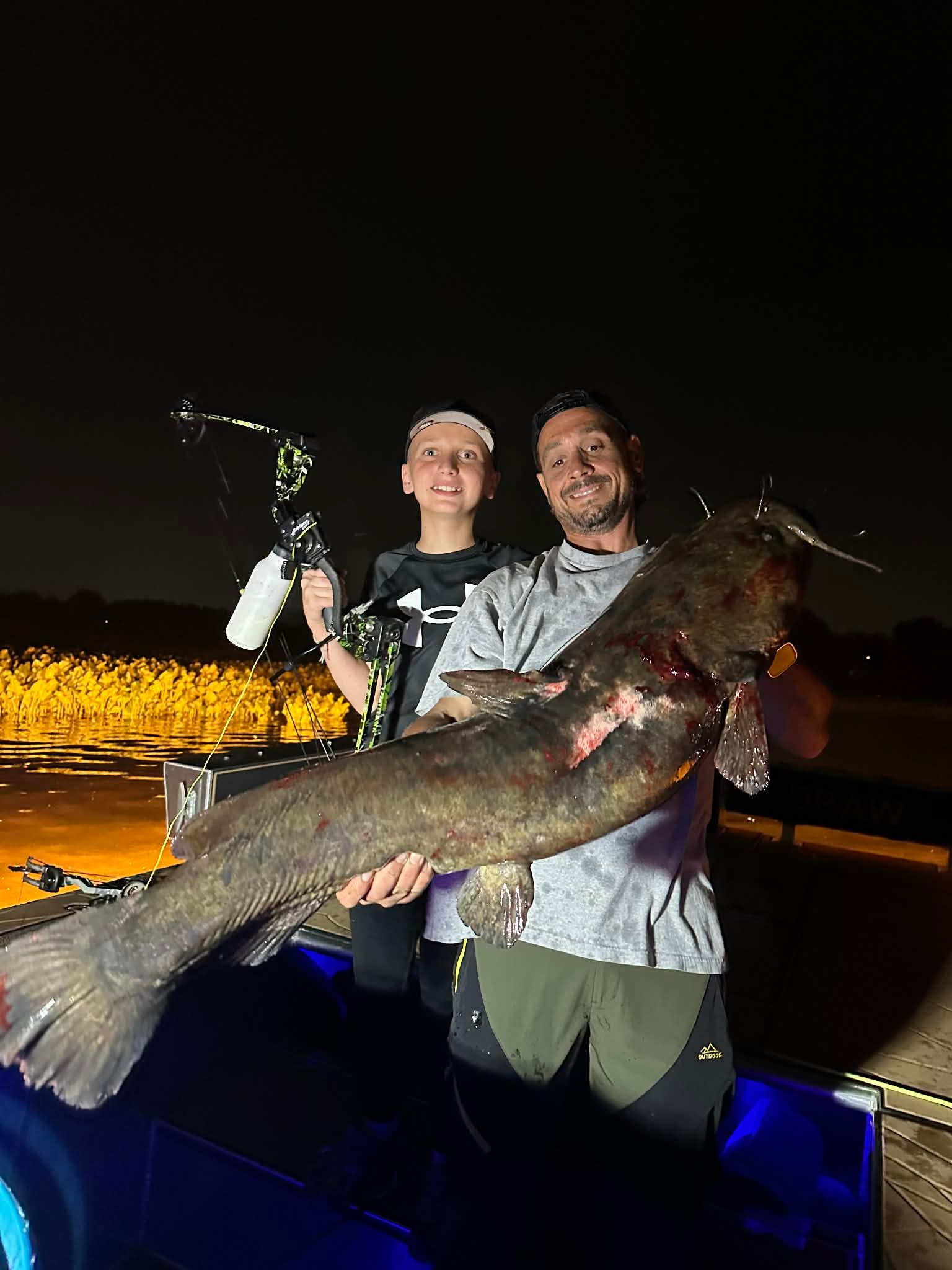 Father and son holding a large flathead catfish caught bowfishing