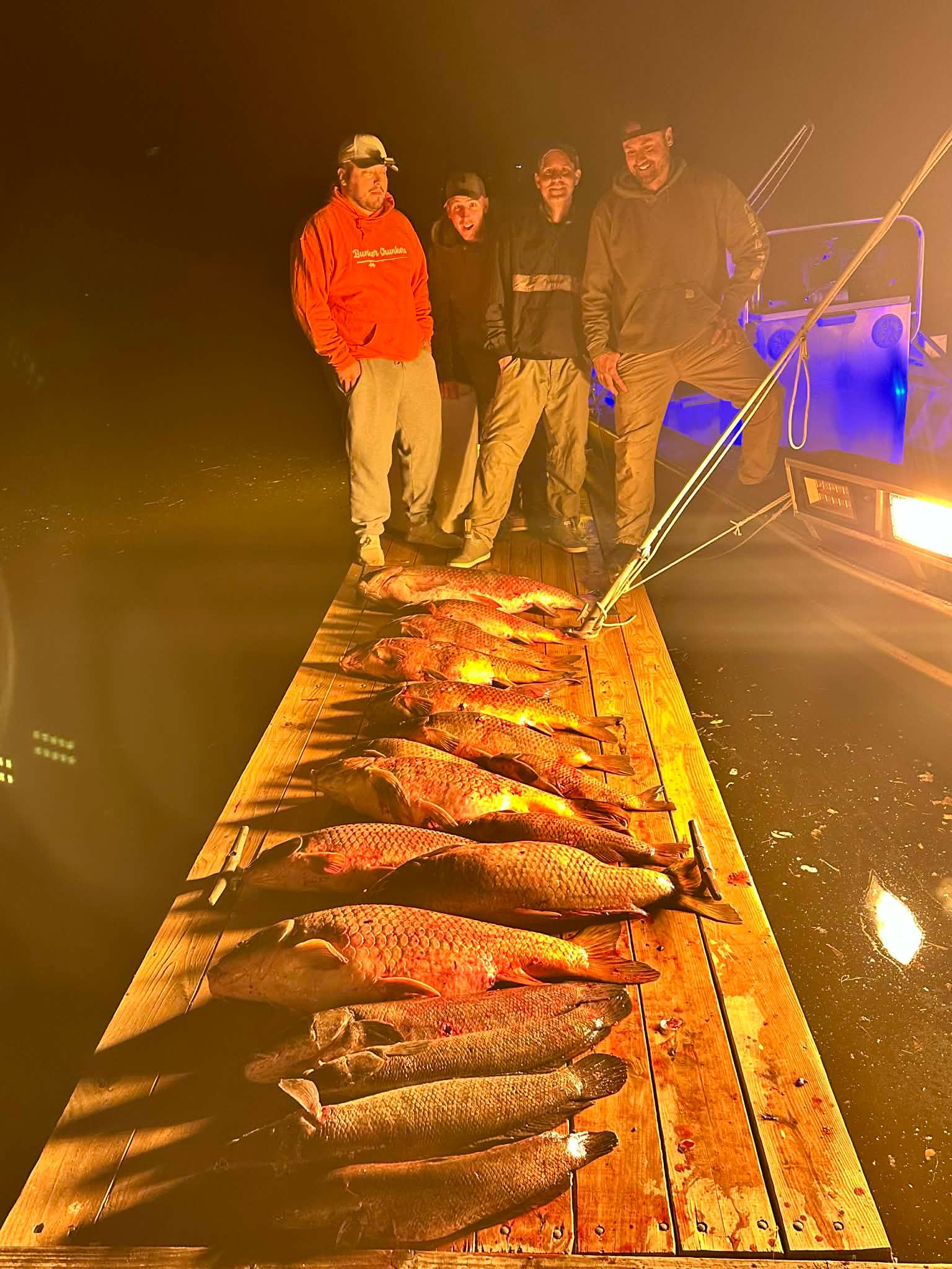 Four anglers standing over a large multi-species bowfishing catch on the dock