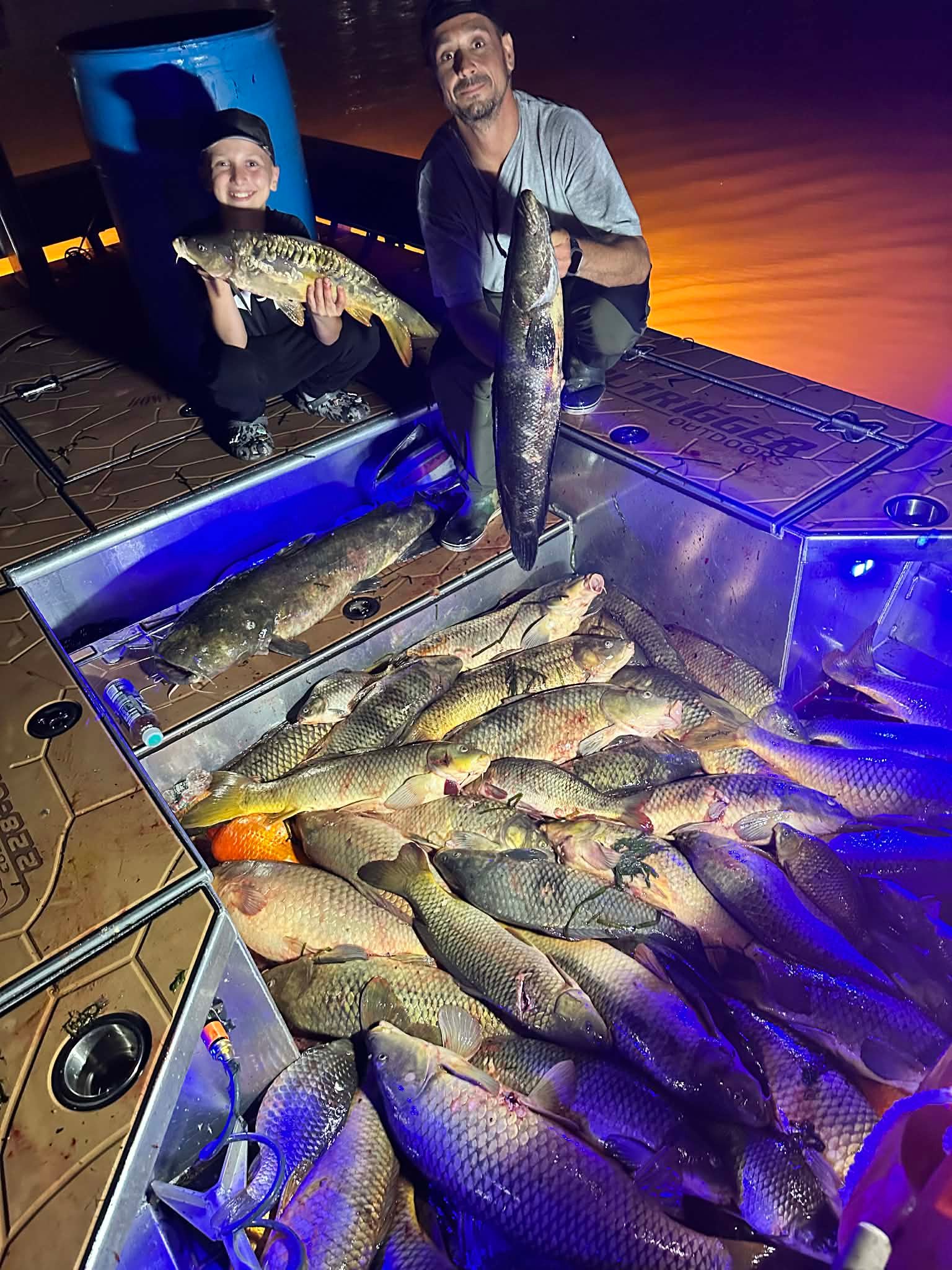 Five anglers standing over a large bowfishing catch laid out on the dock