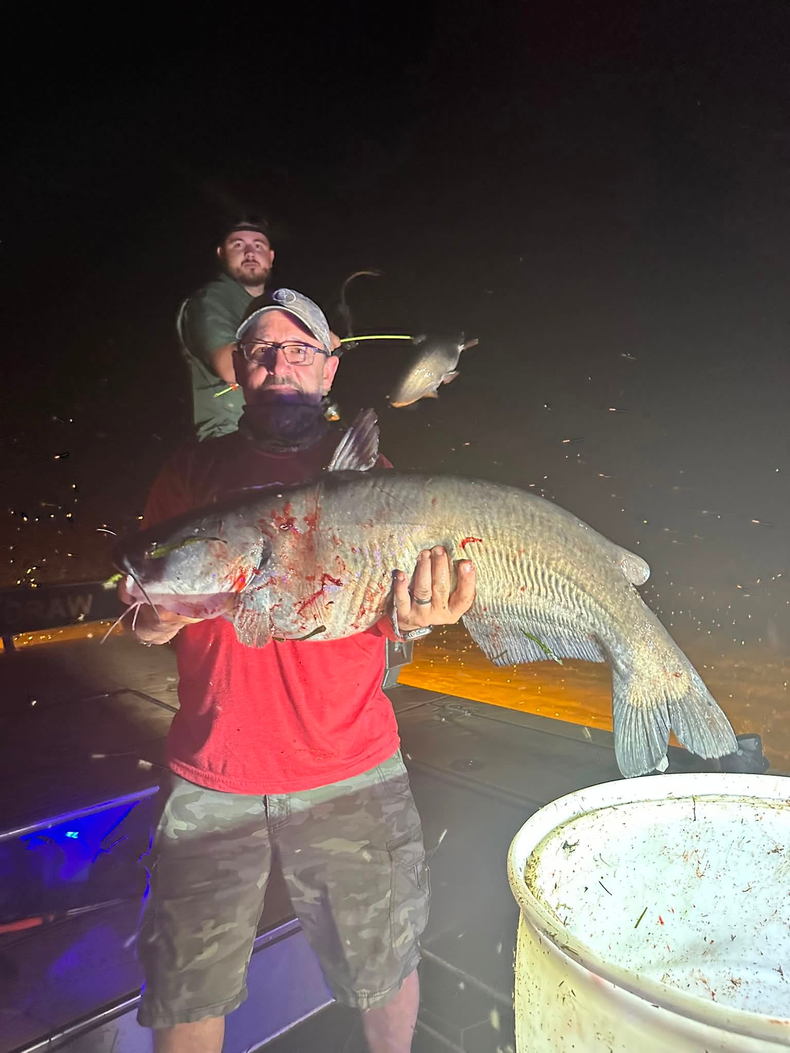 Angler holding a large flathead catfish caught bowfishing at night