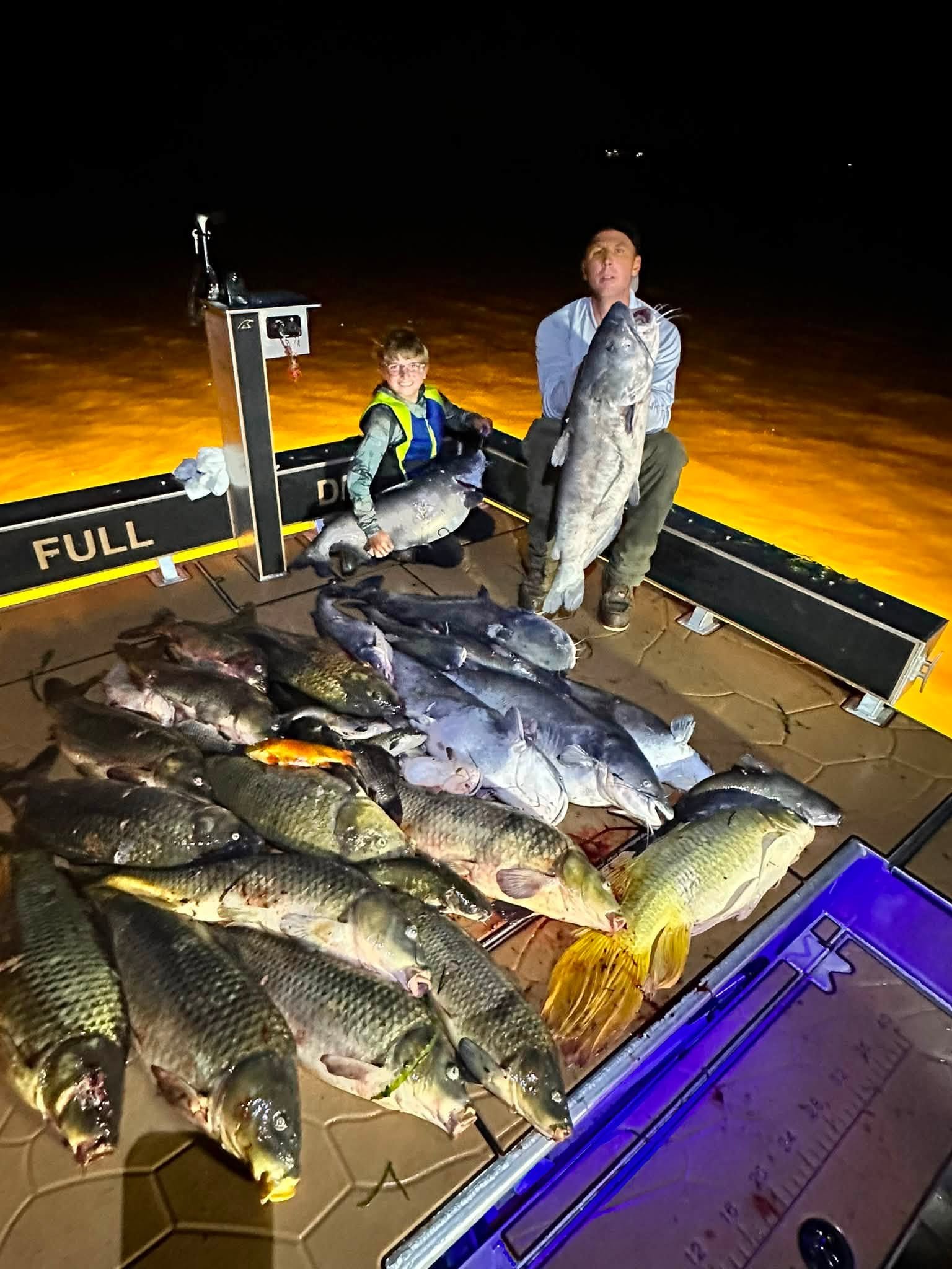 Bowfishing anglers holding bows and carp caught on the Delaware River at night