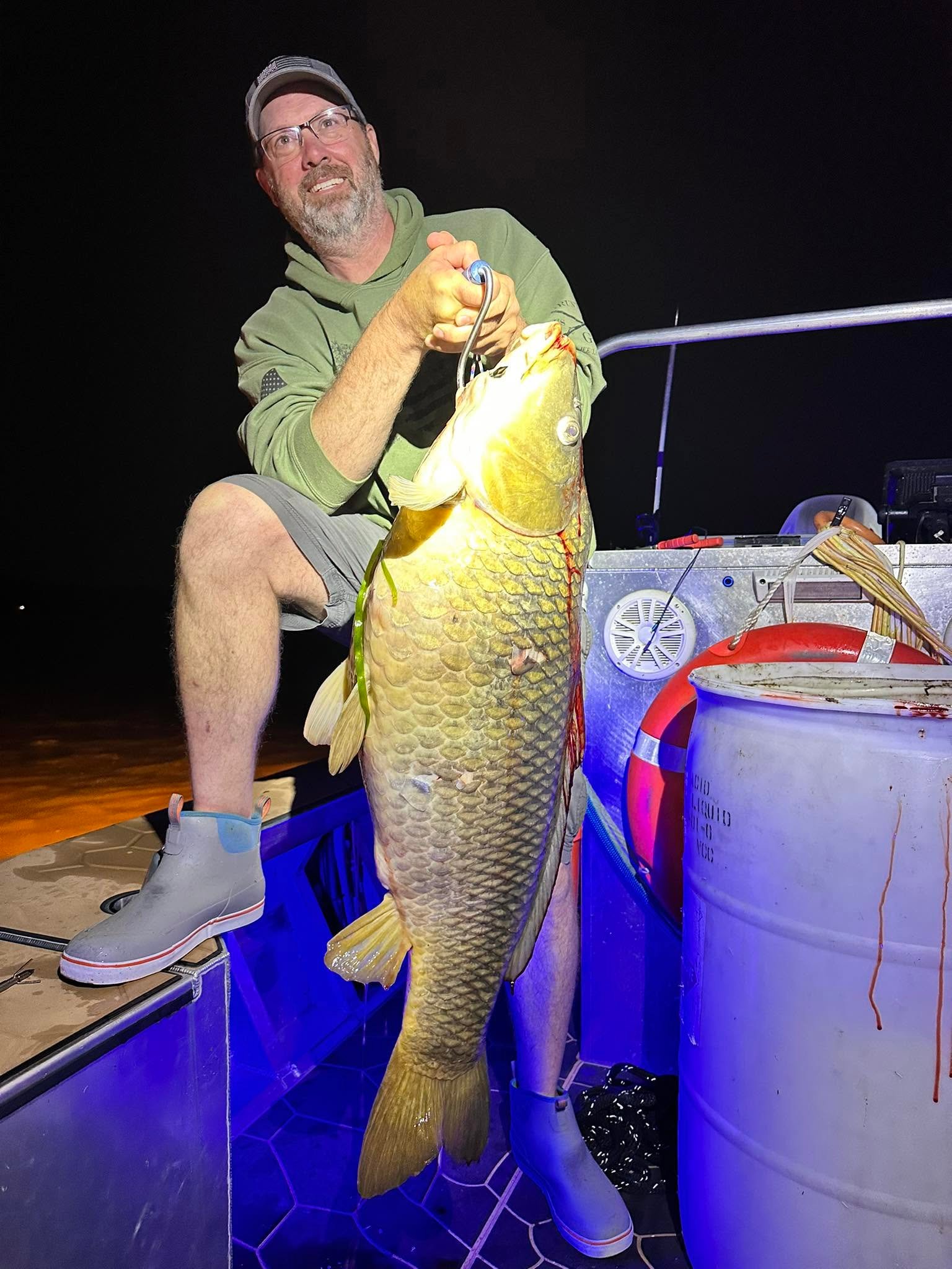 Two anglers each holding two carp on the boat at night