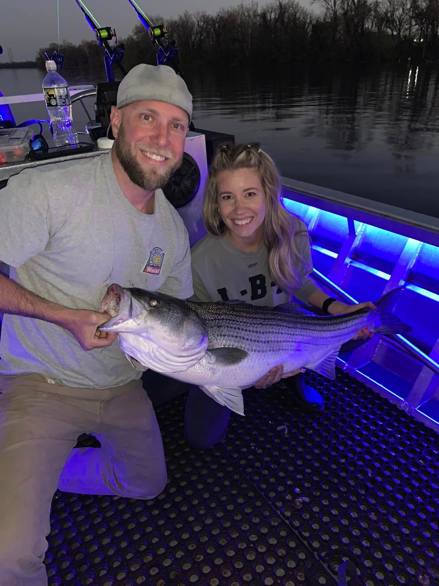 Two anglers holding a striped bass on the boat at dusk